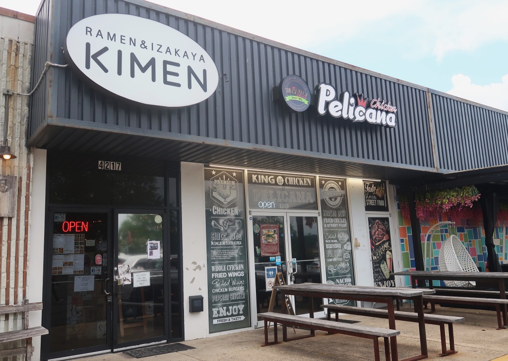 Mặt tiền cũ của Kimen Ramen & Izakaya và Pelicana cạnh các bàn ăn ngoài trời.
